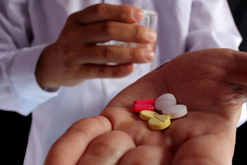 A red, yellow and white pill was placed on the left hand and the right hand held a glass of water to take the pill.