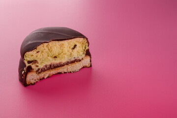 Half of biscuit cookie in chocolate glaze or frosting with jam inside on pink background. Sweet tasty unhealthy snack. Copy space.