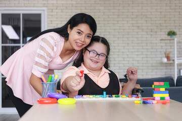 young girl with autism is practicing fun playing with toys at home with his mother. Autistic young students and teachers smiling and looking camera.