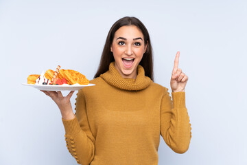 Young caucasian woman holding waffles isolated on blue background pointing up a great idea