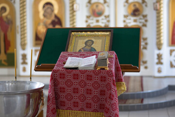 The interior of a Christian church. Prayer table covered with patterned red cloth. Bible, casket, icon and blurred iconostasis in the background.