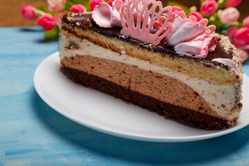 Half of cake on white plate on blue painted background. Sweet bakery with artificial spring flowers