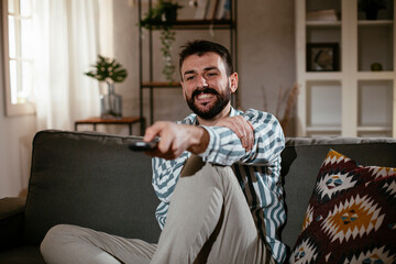 Young man at home. Man sitting in living room watching movie and drinking beer..