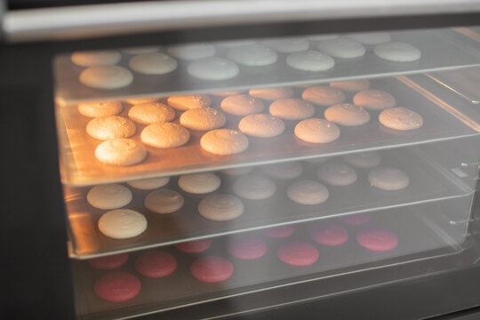 Baking macaroons in the oven. Colorful macarons cookies on baking trays in the oven. The process of making cookies in a confectionery shop. Selective focus
