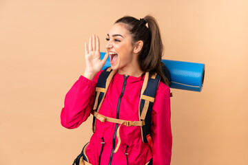 Young mountaineer girl with a big backpacker isolated on beige background shouting with mouth wide open