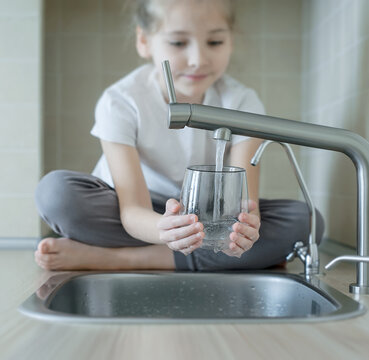 Child is holding a transparent glass. Filling cup beverage. Pouring fresh drink. Consumption of tap water contributes to the saving of water in plastic bottles and to the protection of the environment