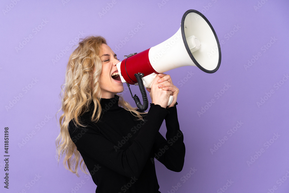 Poster Young blonde woman isolated on purple background shouting through a megaphone