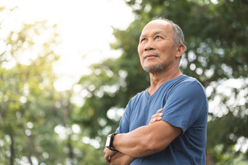 Asian Old man in blue shirt smiling with arms crossed at park outdoor with copy space, Positive...