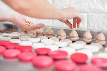 Macarons baking at confectionery shop. Close up of female hands putting hazelnuts on ganache cream on caramel macarons shells on the table