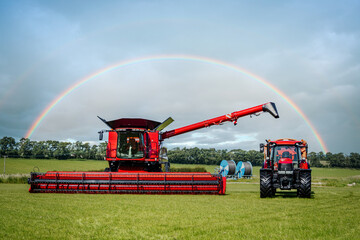 Brand new modern clean combine harvester and shiny red agricultural tractor in rural farm field on...