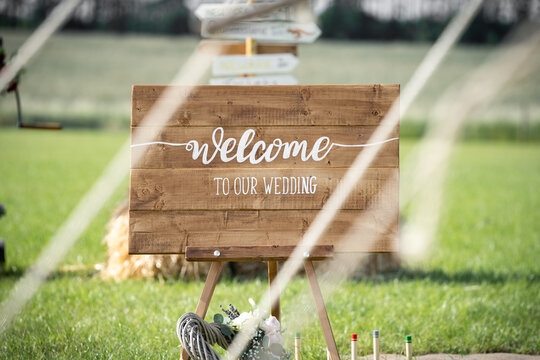 Welcome to our wedding rustic wooden sign with hand painted writing at farm wedding viewed through ropes of tent on bright summers day with farmland behind