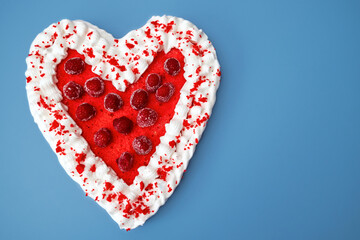 red mousse cake in the shape of a heart on a blue background with beautiful decorated raspberries and cream. Valentine's Day