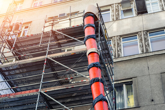 Scaffolding with big red plastic slide chute for rubble debris removal on old historica building facade renewal construction site in city street. Industrial development engineering equipment