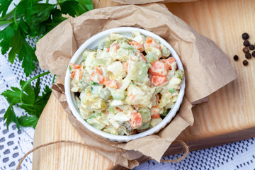 
a portion of Olivier salad with chopped pickles, vegetables, served on a white plate on a cutting board. Spices on the background. View from above