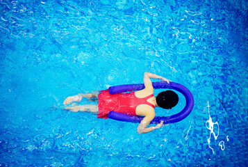 Happy little kid girl learning to swim with pool noodle with coach woman, top view