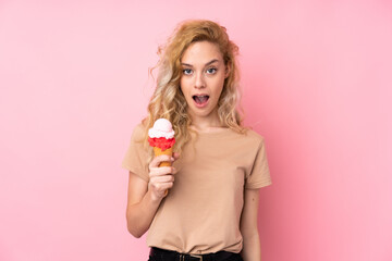 Young blonde woman holding a cornet ice cream isolated on pink background with surprise and shocked facial expression