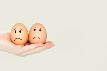 Hand holding two eggs with sad face isolated on white background. Bad emotions and stay together easter concept.