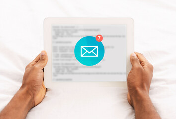 African Man Reading Email Messages On Tablet Lying In Bedroom