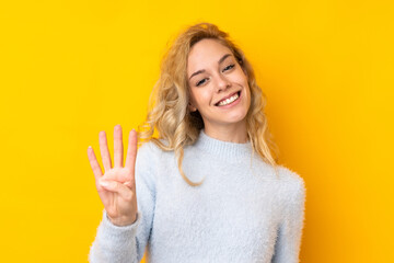 Young blonde woman isolated on yellow background happy and counting four with fingers - obrazy, fototapety, plakaty