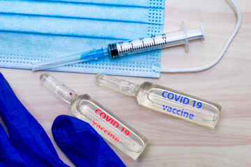 Obraz premium a syringe mask gloves and ampoules labeled covid19 vaccine in blue and red are on the table