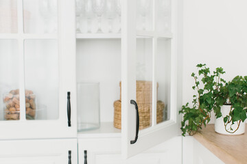 
Opened door of white glass cabinet with clean dishes and decor. Scandinavian style kitchen interior. Organization of storage in kitchen. Selective focus. - obrazy, fototapety, plakaty