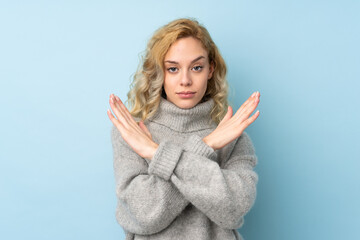 Young blonde woman wearing a sweater isolated on blue background making NO gesture