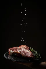 Foto op Canvas Chef hands cooking dry aged wagyu porterhouse beef steak with large fillet piece adding salt and pepper in a freeze motion on black background. vertical image, place for text © Надія Коваль