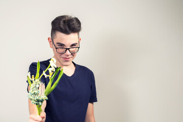 a malicious young man with glasses holds out a bouquet of wilted flowers and smiles. the concept of greed and stinginess. focus on flowers, guy in blur