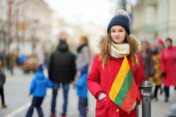 Cute young girl celebrating Lithuanian Independence Day holding Lithuanian flag in Vilnius, Lithuania