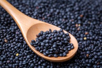 Black beluga lentils in a wooden spoon on black beluga lentils background. Close-up.