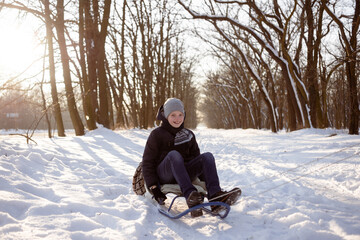 Fototapeta na wymiar portrait of a schoolboy boy playing outdoors with snow. Happy child sits on a sled on a winter day in a park or forest. Copy space.