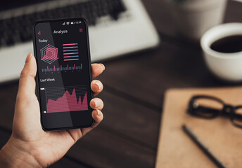 Woman using smartphone with online statistic and data analytics graphs on screen