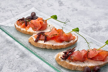 three bruschetta with trout, salmon, cream cheese and microgreen on a glass plate on a white background