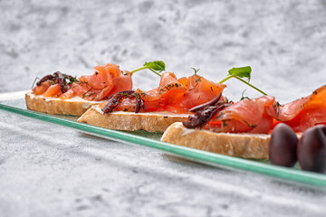 three bruschetta with trout, salmon, cream cheese and microgreen on a glass plate on a white background