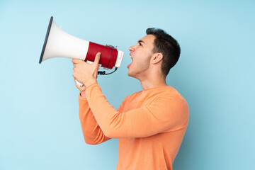 Young caucasian handsome man isolated on blue background shouting through a megaphone