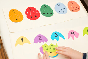 Different color paper eggs with numbers on one part and the equivalent amount of dots on other. Easter theme game, find other side of figure.