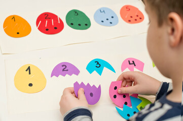 Different color paper eggs with numbers on one part and the equivalent amount of dots on other. Easter theme game, find other side of figure.