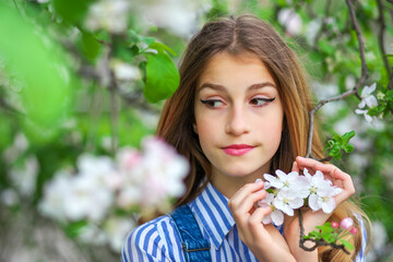 Fototapeta premium Pretty teen girl are posing in garden near blossom tree with white flowers. Spring time