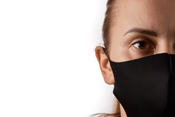 Horizontal close up portrait of a young european woman with brown eyes wearing black face mask, covering her nose, looking straight at camera, isolated over white background, copy space on the left.