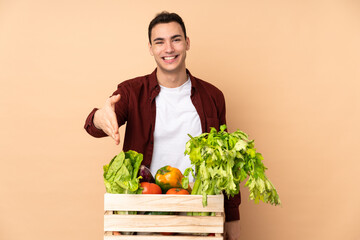 Farmer with freshly picked vegetables in a box isolated on beige background shaking hands for closing a good deal