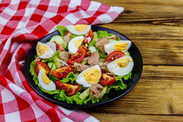 Tasty tuna salad with eggs, lettuce and fresh vegetables on wooden table