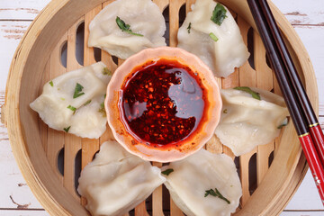 Home style dim sum dumpling in bamboo steamer chopsticks chili flake oil sauce on rustic wooden...