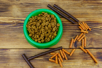 Dog delicacy food and feed in green plastic bowl on wooden background. Top view. Dog care concept