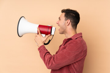 Young caucasian handsome man isolated on beige background shouting through a megaphone