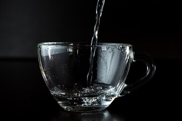pouring water into a glass. transparent cup with water on a dark background.