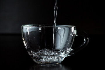 pouring water into a glass. transparent cup with water on a dark background.