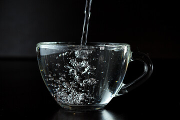 pouring water into a glass. transparent cup with water on a dark background.
