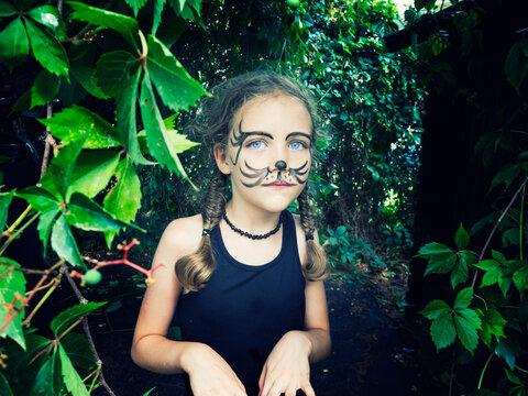 Portrait of a girl with tiger face paint standing in a garden, Italy