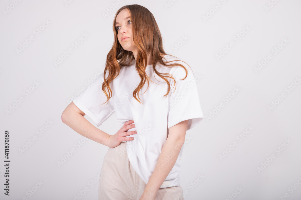 Wall mural young beautiful redhead woman in basic clothes white t-shirt and beige pants. attractive woman posin