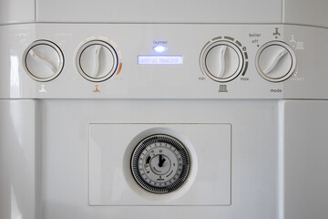 Gas heater combi boiler close up on dials. Set for winter settings and displayed over LCD. Burner light is on. 